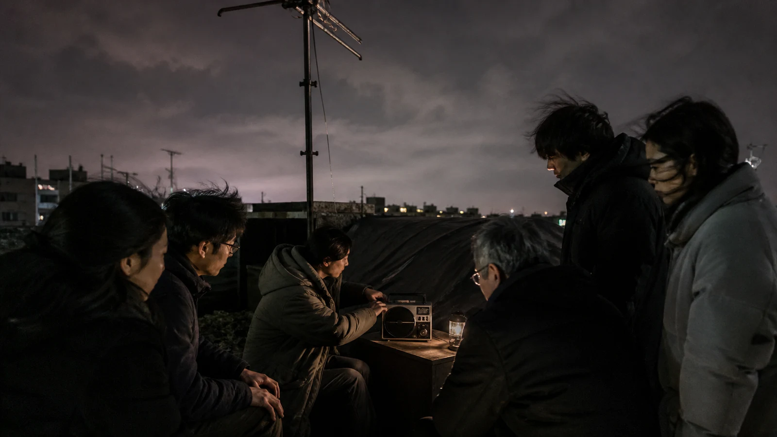 夜の屋上でラジオを囲み、声に耳を傾ける住民たち